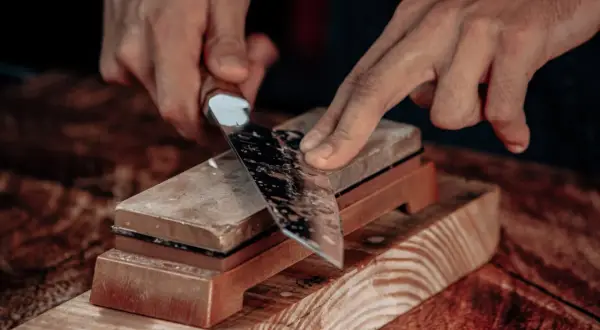 Manos afilando un cuchillo con una piedra de afilar. Aprende como afilar cuchillos con afilador para un corte perfecto.