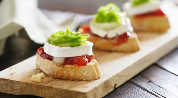 Deliciosos pinchos y tapas originales: rebanadas de pan con queso de cabra, mermelada de pimientos y cebolla morada.