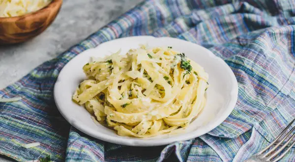 Pyszny sos do makaronu z parmezanem i ziołami na talerzu, obok miska z serem i widelcem.