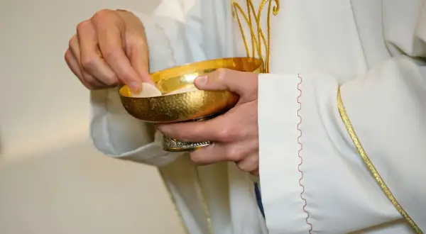 Kapłan podaje hostię z kielicha. Poważne grzechy po których nie można przystąpić do komunii wymagają spowiedzi.