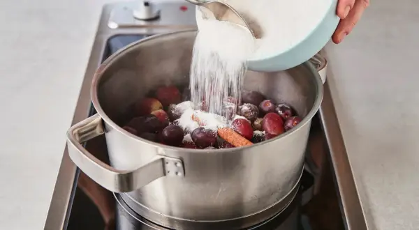 Zucker wird zu Trauben und Zimt in einem Topf gegeben, um köstliche Weintrauben Marmelade herzustellen.