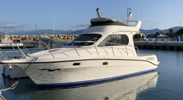 Yacht Intermare 30 ormeggiato in porto, con riflessi sull'acqua calma. Montagne sullo sfondo.