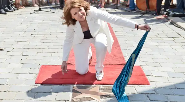 Halina Frąckowiak klęczy na czerwonym dywanie, odsłaniając gwiazdę z napisem. W ręku trzyma turkusową wstęgę, jakby symbolizującą tekst "Papierowy Księżyc".