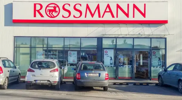 Elegancka fasada drogerii Rossmann z czerwonym logo i zaparkowanymi samochodami.