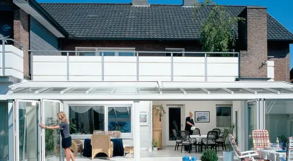 Nowoczesna dobudowa balkonu w domu jednorodzinnym. Szklany ogród zimowy z rozsuwanymi drzwiami i widokiem na taras.