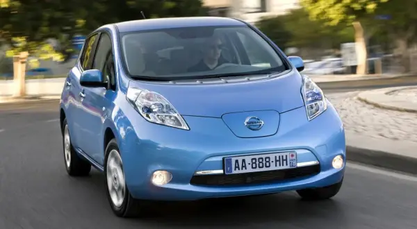 Un coche azul Nissan Leaf, uno de los coches mas fiables de segunda mano, circula por una carretera.