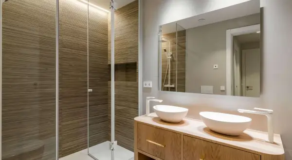 Baños pequeños con encanto: ducha con paredes de madera acanalada y tocador de madera con dos lavabos blancos.