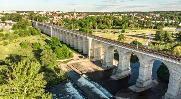 Kamienny wiadukt kolejowy nad rzeką, z miastem w tle. Bolesławiec atrakcje, które zachwycają.
