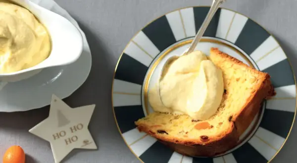 Una fetta di panettone con abbondante crema al mascarpone, servita su un piatto decorato. Un'idea golosa per le feste.