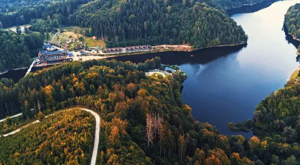 Malownicze jezioro w Zagórzu Śląskim otoczone jesiennymi lasami. W oddali widać zabudowania ośrodka wypoczynkowego.