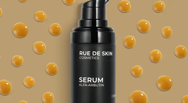Czarny flakonik serum z alfa-arbutyną, otoczony kropelkami o bursztynowym kolorze.