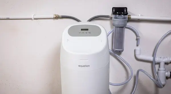 Instalación de descalcificador Equation con filtro de agua. Sistema de tuberías blancas y mangueras grises conectadas a la unidad.
