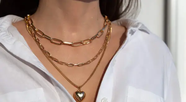 Tres collares dorados en capas, uno con un corazón, lucen perfectos con el escote de una camisa blanca.