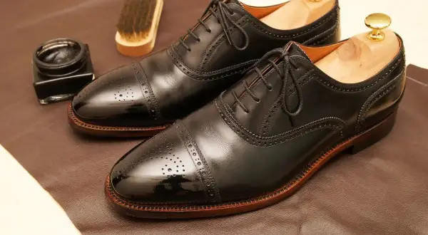Paire de richelieus noirs brillants, prêts pour un glacage chaussure parfait. Pot de cirage et brosse à proximité.