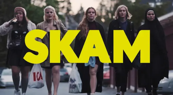 Fem tjejer går på gatan, med stora gula bokstäver som bildar ordet SKAM. En av dem dricker ur en flaska.