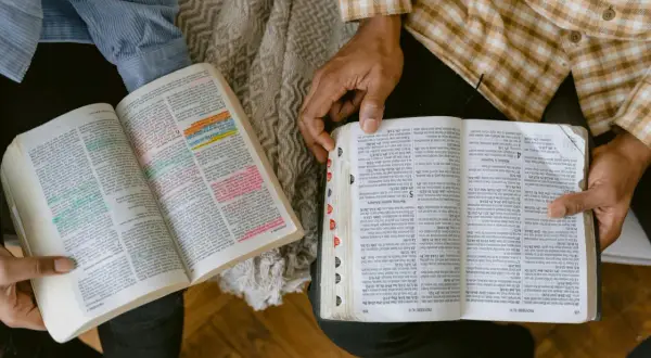 Dwie osoby studiują Biblię, analizując podział ksiąg biblijnych. Widać fragmenty z kolorowymi zakreśleniami.