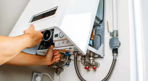 Tecnico che regola la pressione del gas dello scaldabagno, mostrando i collegamenti idraulici e il pannello di controllo.