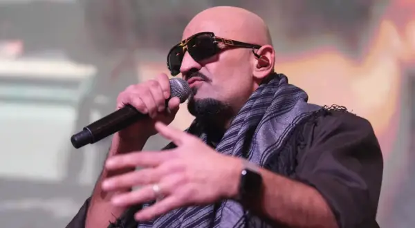 Ein bekannter Rapper mit Sonnenbrille und Schal spricht ins Mikrofon, während er gestikuliert.