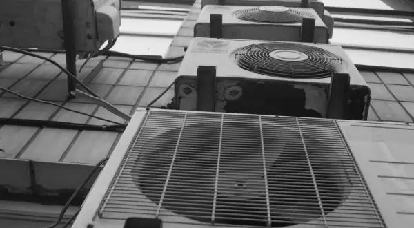Vue en contre-plongée de plusieurs unités de climatisation extérieures, dont une pompe à chaleur triphasé, alignées sur un mur.