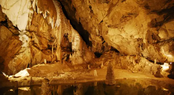 Wnętrze jaskini z naciekami i stalagmitami, odbijającymi się w wodzie. Tajemnicze piękno Tatr Bielskich.
