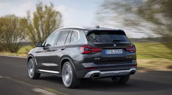 Ciemnoszary BMW X3 xDrive pędzi po drodze, otoczony zielenią i rozmazanymi drzewami.