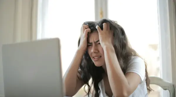 Kobieta z rękami we włosach, patrząca na laptopa z wyrazem frustracji. Czasem czuję, że moje życie to porażka.