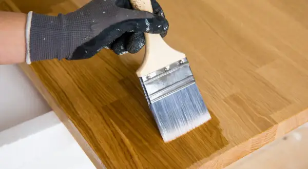 Maintenant, peut on vernir après huile de lin ? Un pinceau applique une couche transparente sur un plateau en bois.