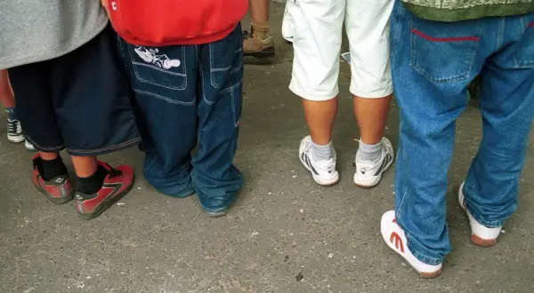 Luźne spodnie, szerokie nogawki i sportowe buty – to wszystko w stylu hip hop. Grupa młodych ludzi w luźnych ubraniach.