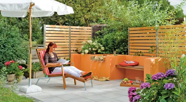 Entspannter Garten mit selbst gebautem Wasserfall. Eine Frau liest unter einem Sonnenschirm.