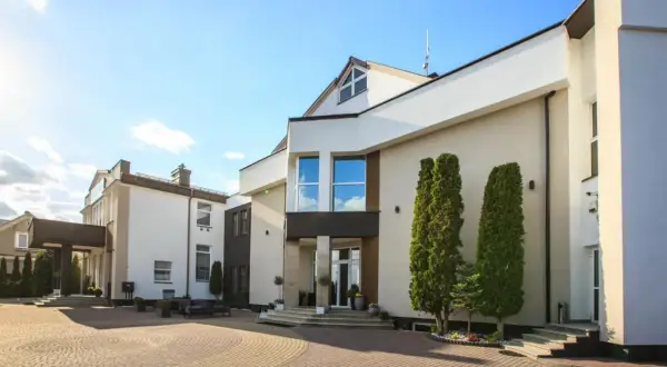 Nowoczesny budynek hotelu Santana Białystok z podjazdem z kostki brukowej i zielenią.