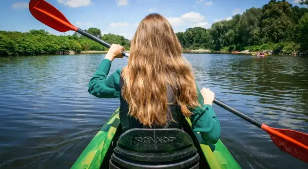 Dziewczyna wiosłuje kajakiem po spokojnej rzece, ciesząc się piękną pogodą. Idealne miejsce na spływy kajakowe Śląsk.