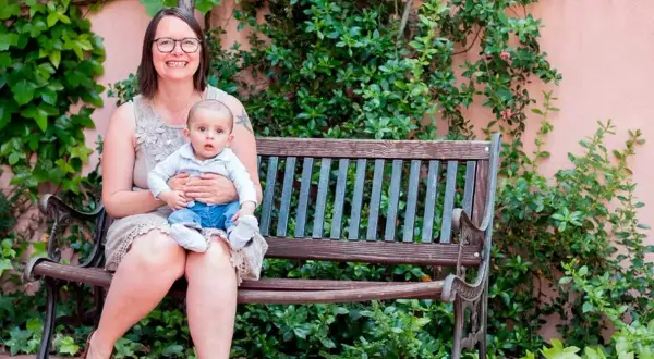 Madre sonriente abraza a su bebé en un banco. Un ejemplo de los hermosos testimonios de hijos nacidos por ovodonación.