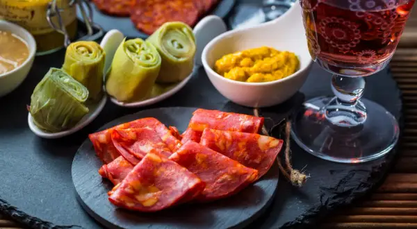 Leckere Tapas Ideen: Chorizo, eingelegte Artischocken und Senf mit einem Glas Rotwein.