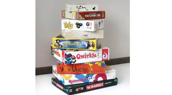 Stos pudeł z grami planszowymi, idealnymi na rodzinne wieczory. Wśród nich "Splendor", "Qwirkle", "Ubongo" i "Scrabble" – świetna gra dla seniorów.