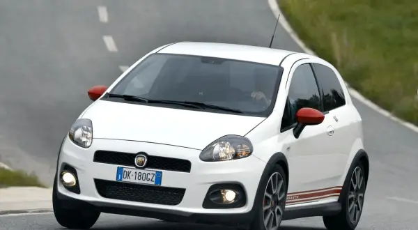 Biały Fiat Punto Abarth z czerwonymi lusterkami i paskami na boku, jadący po krętej drodze.