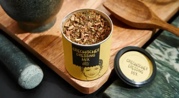 Dose mit Gewürzmischung für original griechischer salat dressing, daneben Mörser und Holzschale.