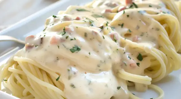 Cremige Spaghetti Carbonara mit Speckwürfeln und Petersilie, serviert auf einem weißen Teller.
