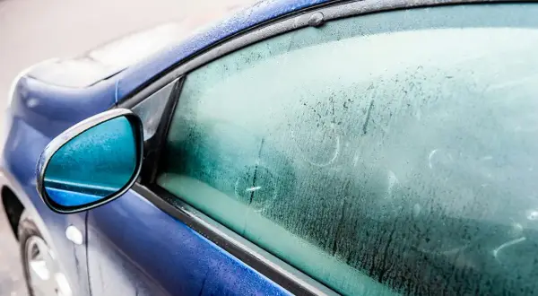 En blå bil med frost på sidorutan. Frågan "hur får man bort imma i bilen" är relevant när det är kallt ute.