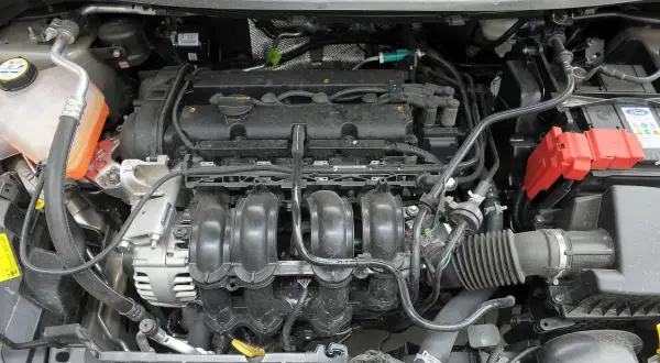 Silnik Ford Fiesta 2011 z widocznym kolektorem dolotowym, alternatorem i akumulatorem.