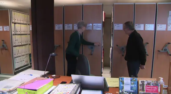 Deux personnes devant des rayonnages d'archives mobiles.