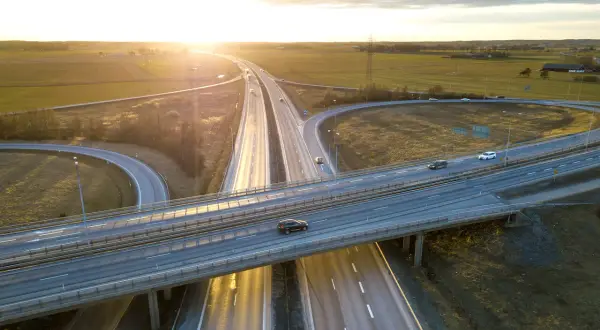 Widok z lotu ptaka na węzeł autostradowy o zachodzie słońca, z samochodami na jezdni.