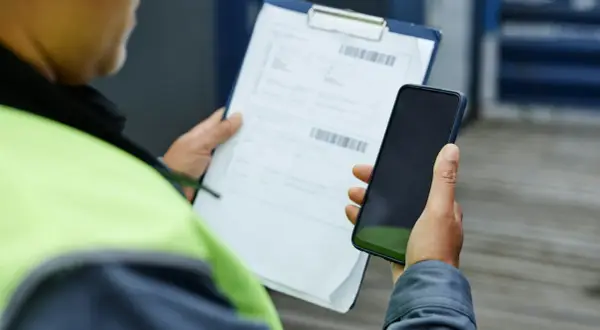 Pracownik w kamizelce odblaskowej trzyma telefon i dokumenty. Zastanawia się, czy warto złożyć skargę do PIP.