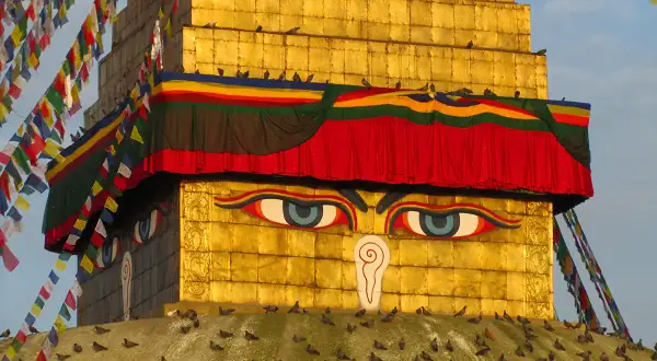 Złota stupa z oczami Buddy, ozdobiona kolorowymi flagami modlitewnymi. Warto odwiedzić takie miejsca święte w buddyzmie w Nepalu i Indiach.