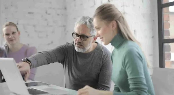 Uomo della generazione boomer spiega qualcosa su un laptop a una collega.