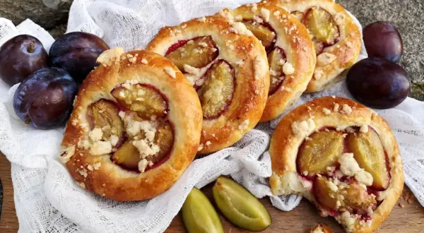 Pyszne drożdżówki ze śliwką, posypane kruszonką, prezentują się apetycznie obok świeżych śliwek.