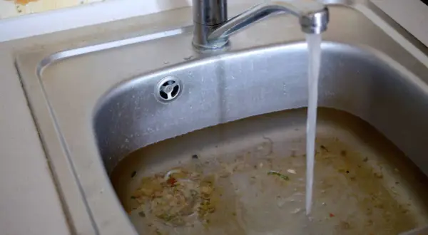 Verstopfter Abfluss im Haus? Salz als Hausmittel könnte helfen. Das Spülbecken ist voller Essensreste und steht unter Wasser.