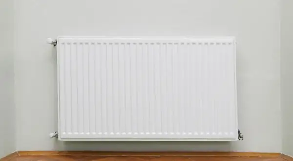 Radiatore bianco moderno su parete chiara, con parquet. Utile per calcolare quanti elementi termosifoni per mq.