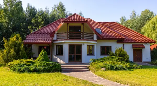 Urokliwa agroturystyka w dolinie stawów. Biały dom z czerwoną dachówką, otoczony zielenią, zaprasza na wypoczynek.