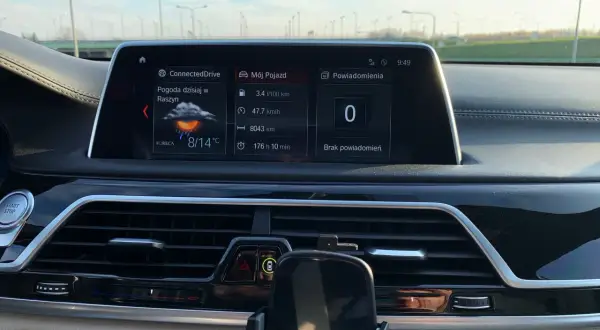 Wnętrze BMW hybryda: ekran z pogodą w Raszynie (8/14°C), spalaniem 3.4l/100km i przebiegiem 8043km.