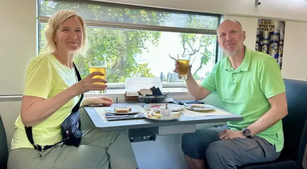 Ett par skålar med öl på ett tåg till München. De njuter av en måltid med bröd, ost och charkuterier medan landskapet susar förbi utanför fönstret.